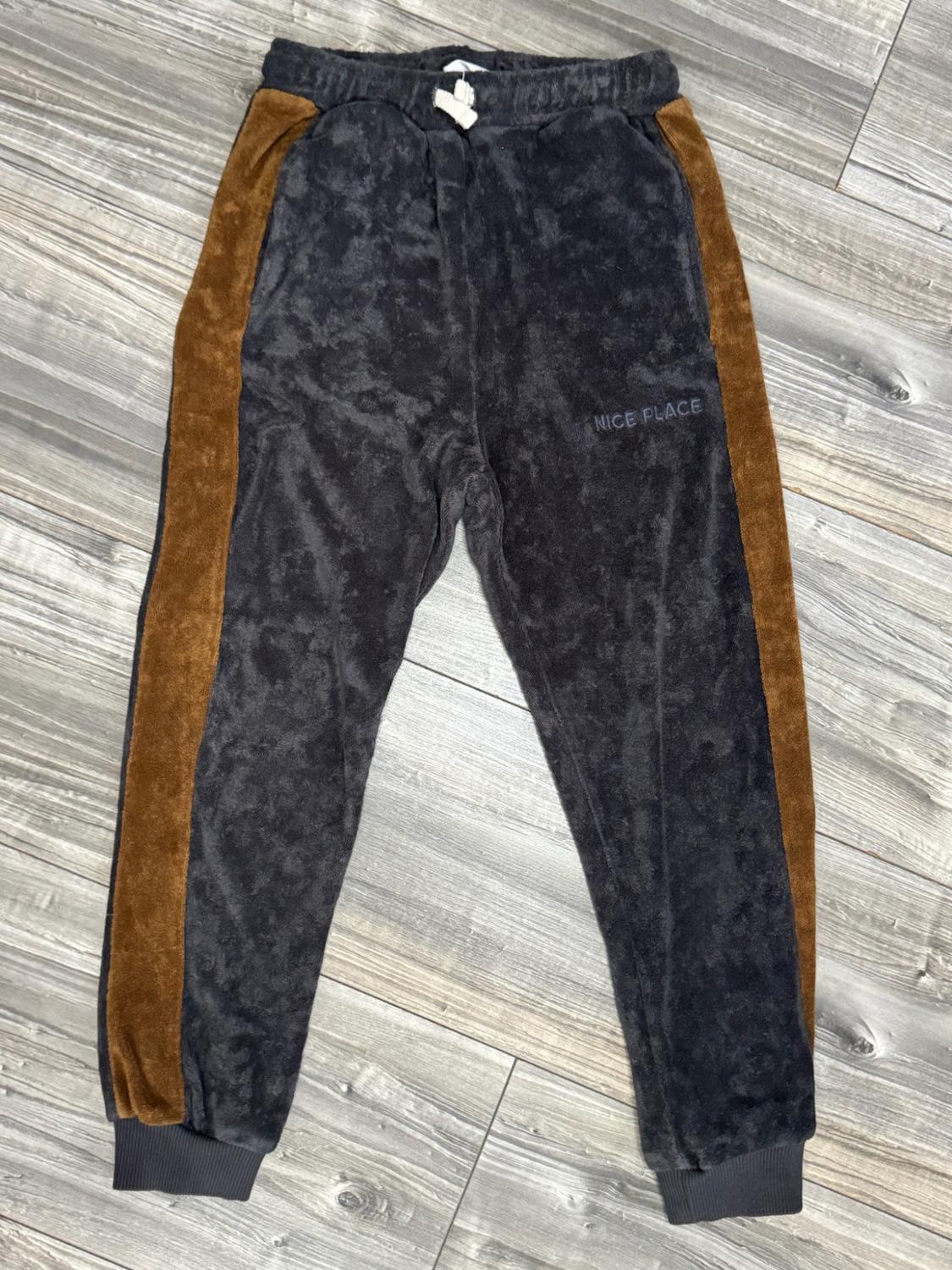 Dark grey trousers with brown side stripes and the text NICE PLACE. Elasticated waist with a white drawstring, on a wooden floor.