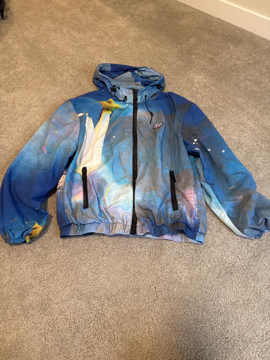 Hooded jacket with a galactic design in blue tones and star details, on a gray carpet.