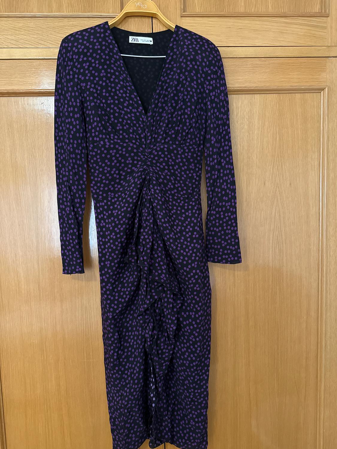 Long-sleeved maxi dress with purple polka dot print on a black background, hanging on a wooden hanger.