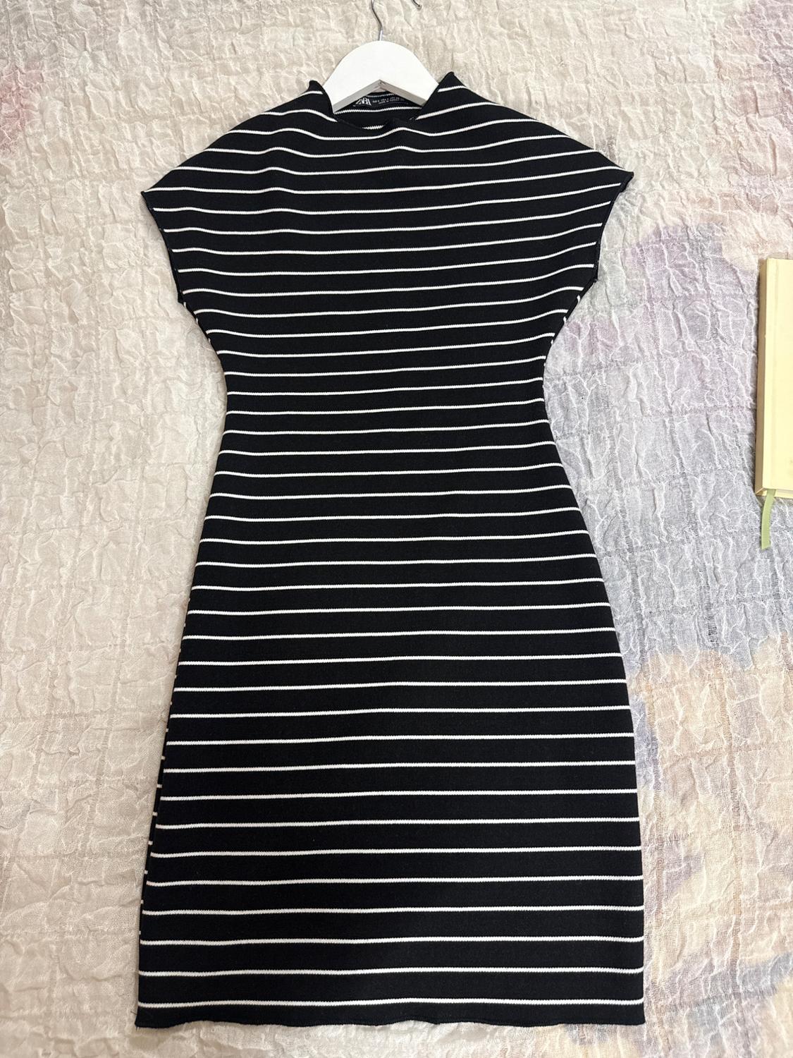 Black dress with white horizontal stripes, high neck and short sleeves on a white hanger, against a light-coloured fabric.