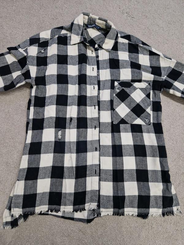 Front view of a black and white checked shirt with a chest pocket and frayed edges.