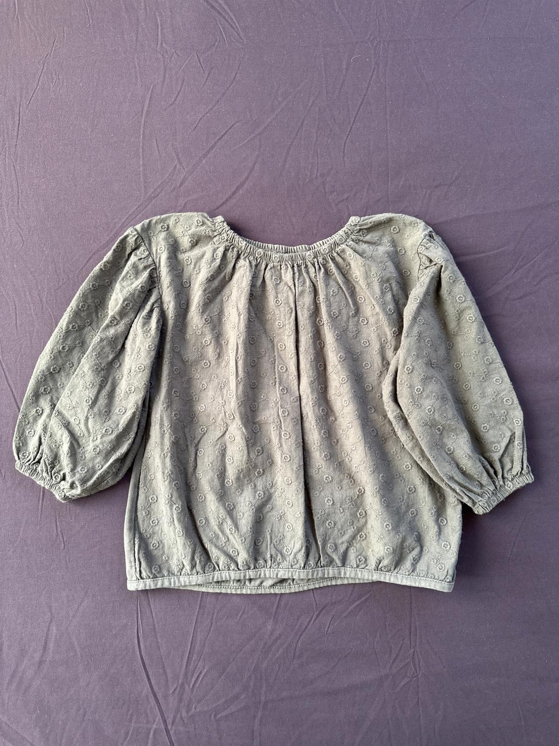 Front view of a green blouse with long puffed sleeves and floral embroidered details.