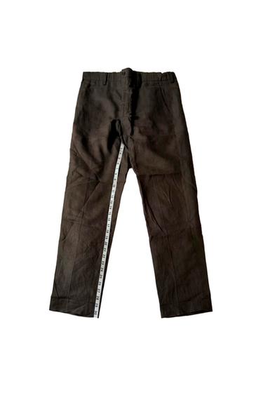 Dark brown trousers on a white background, with a tape measure extended along the inseam.