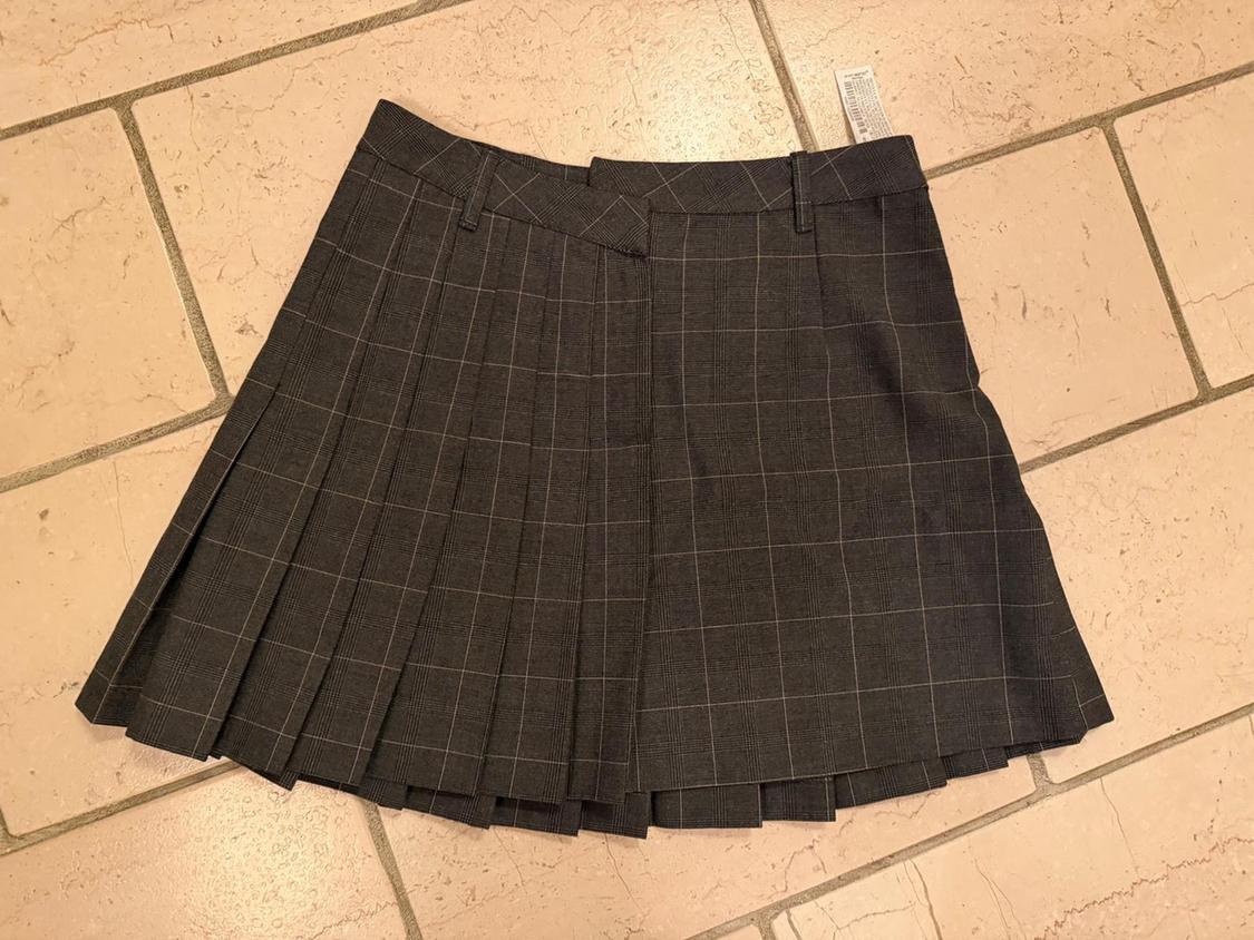 Grey pleated short tartan skirt, placed on a beige tiled floor. Label visible at the top.