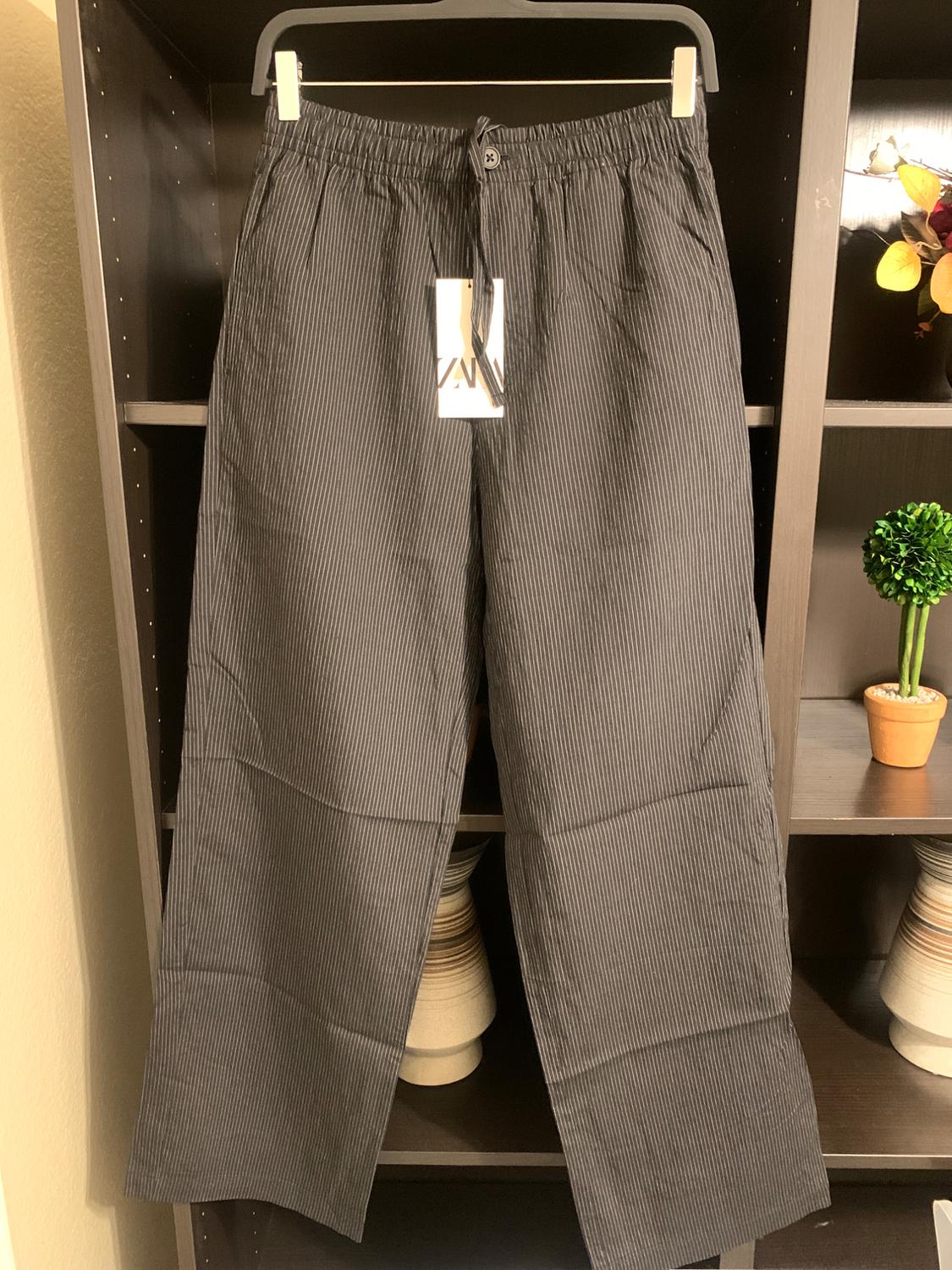 Grey striped trousers hanging on a hanger inside a dark wardrobe. Visible label on the waistband with adjustable drawstring.