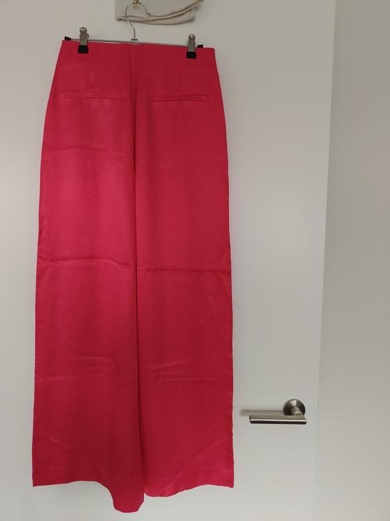 Fuchsia wide-leg trousers hanging on a hanger over a white door with a silver handle.