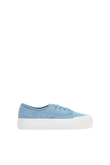 Light blue trainer with laces and a thick white sole on a white background. Simple and modern design.