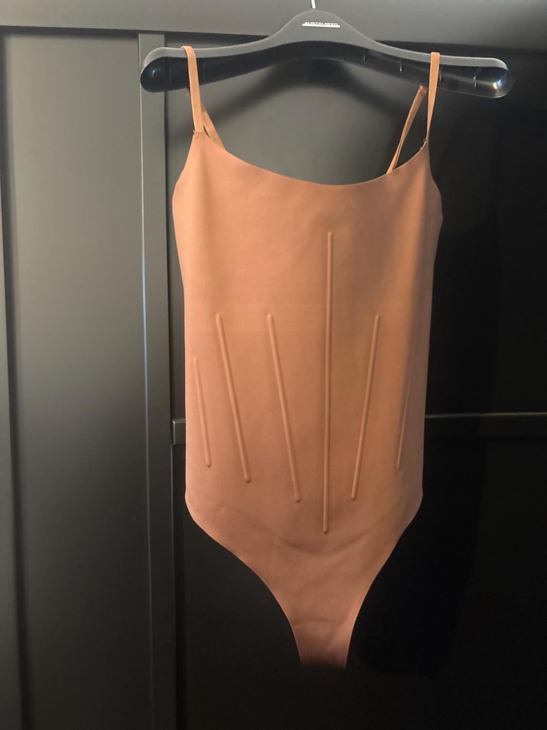 Light brown bodysuit with thin straps and raised vertical seams, hanging on a black hanger with the text AUSTIN REED.