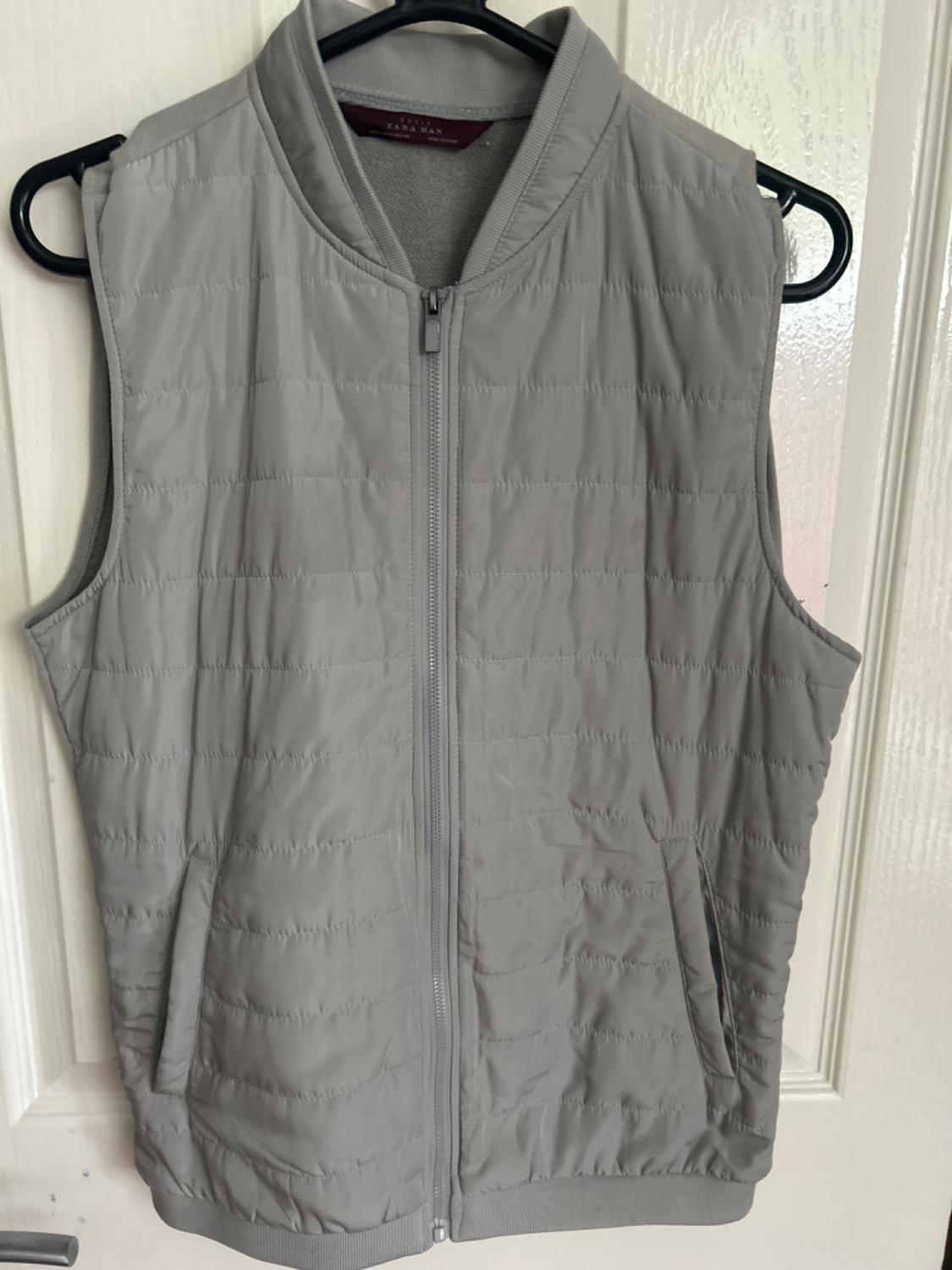 Front view of a grey gilet with a zip and side pockets.