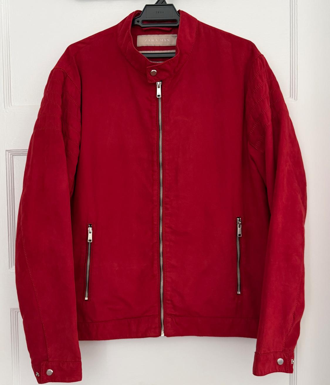 Red jacket with zippers and a buttoned collar, hanging on a hanger over a white door. Inside label with the text ZARA MAN.