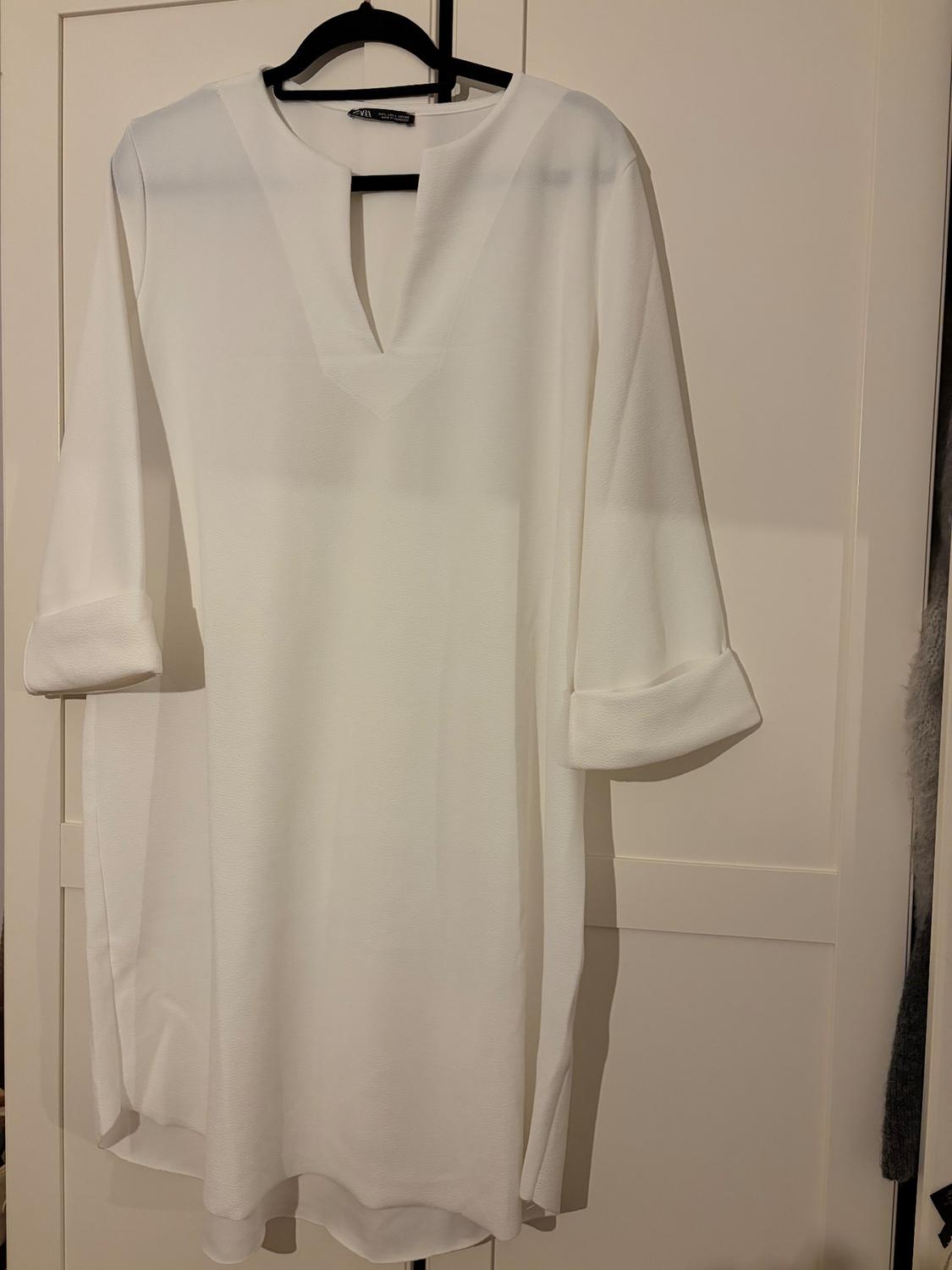 White long-sleeved dress hanging on a black hanger over a white door. Simple design with a V-neck.