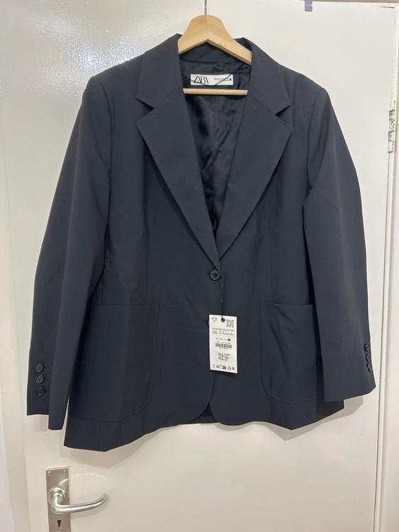 Black suit jacket hanging on a wooden hanger, with visible tag. White door background with silver handle.