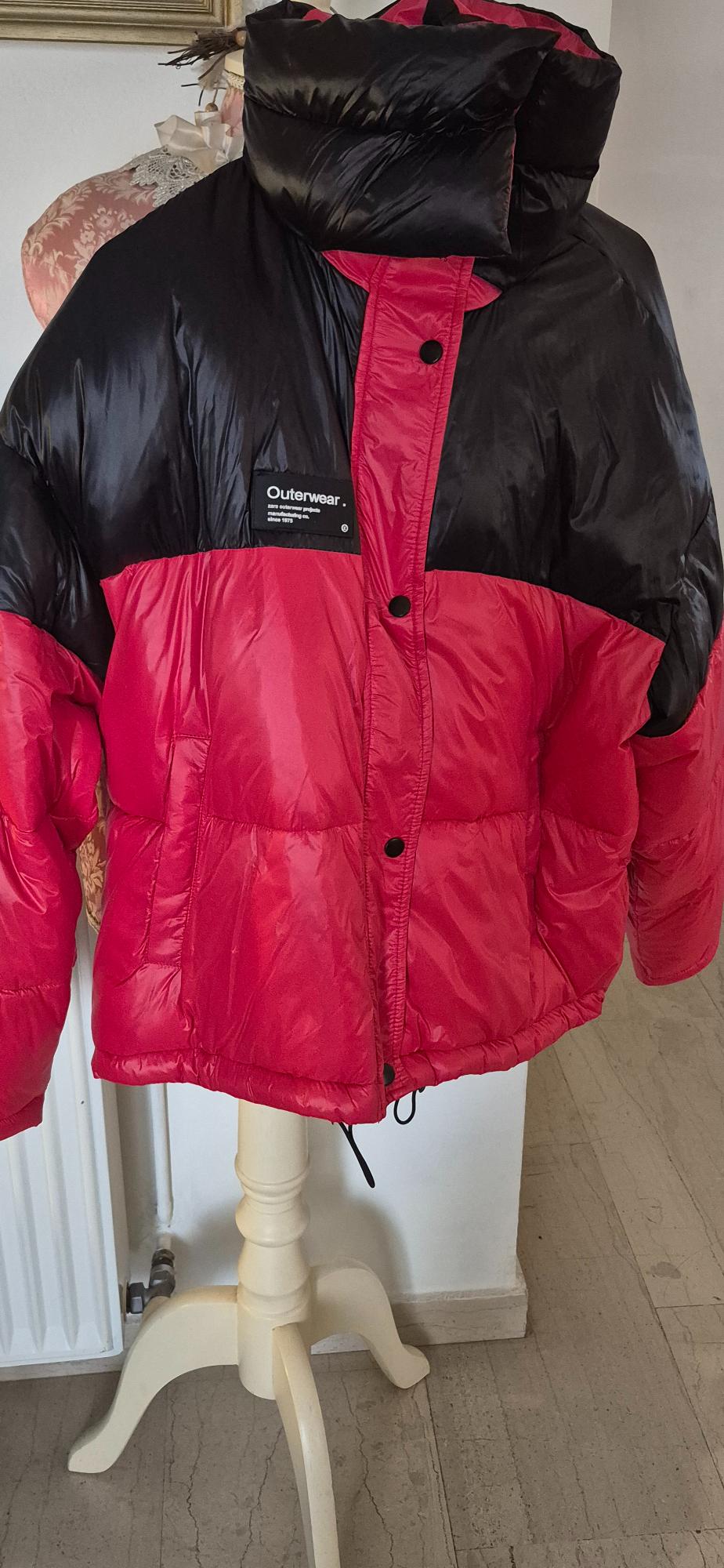 Red and black padded jacket hanging on a white coat rack. Visible text: "Outerwear. 100% outdoor products since 1975".