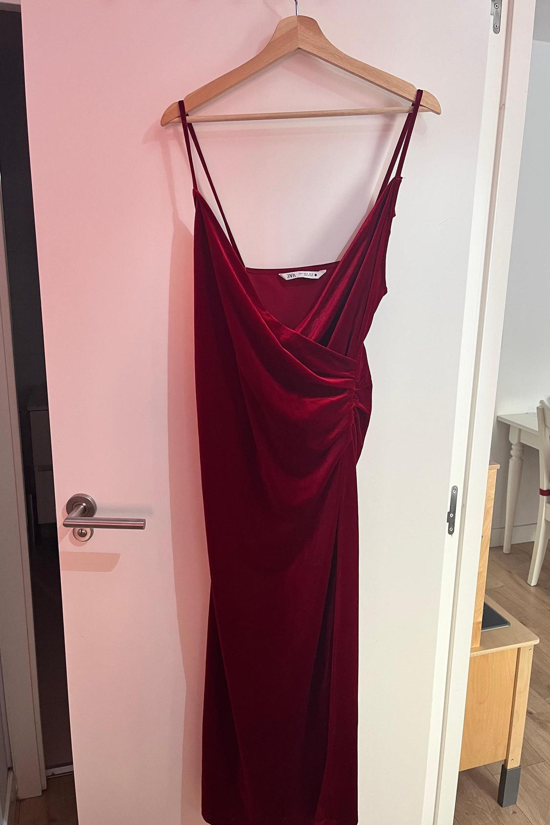 Front view of a red dress with thin straps and side draping, hung on a hanger.
