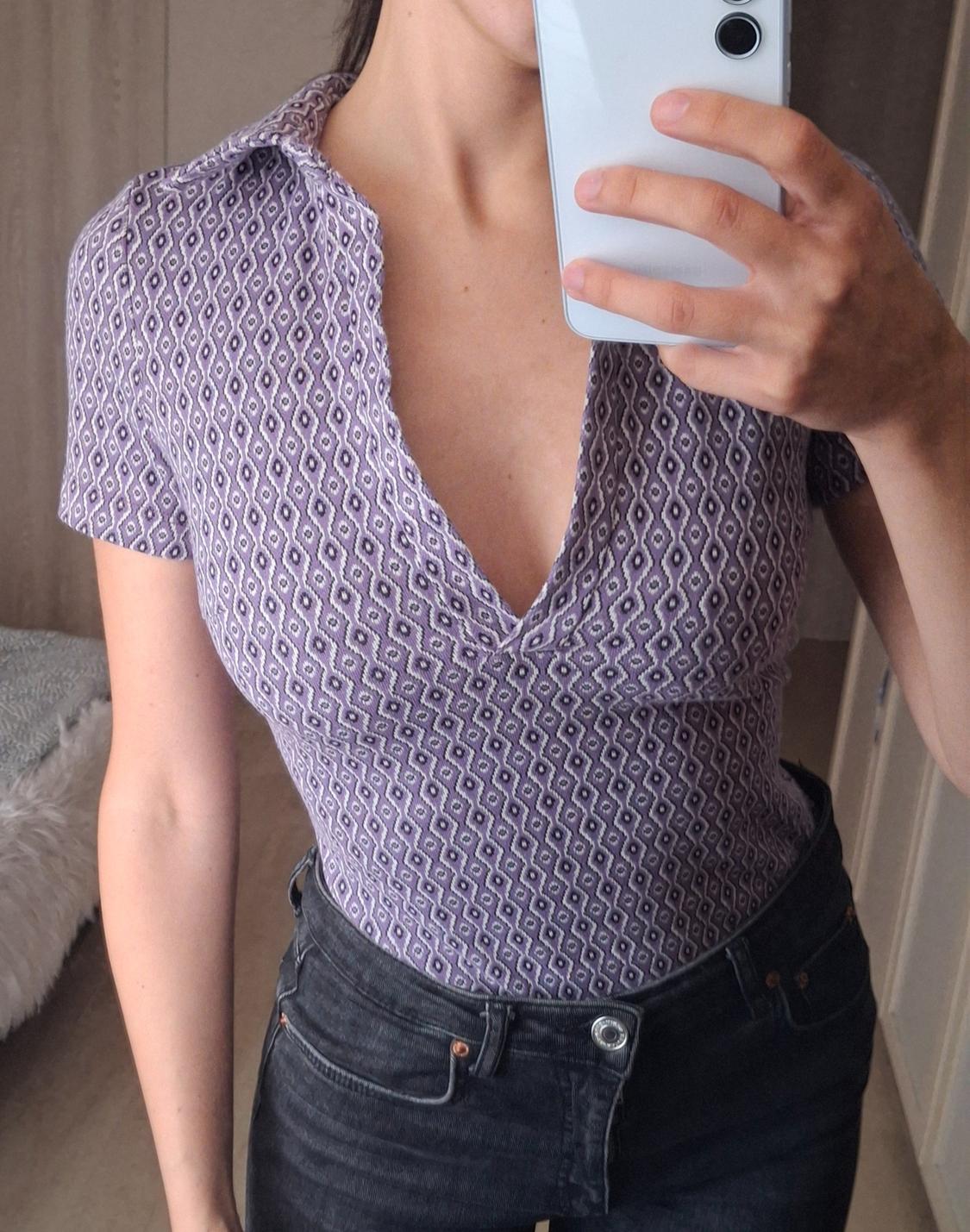 Woman in a purple geometric print V-neck blouse, taking a selfie in the mirror. She is wearing dark trousers.