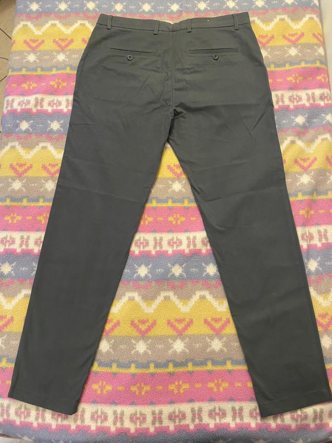Grey dress trousers with buttoned back pockets, placed on a colourful blanket with geometric patterns.