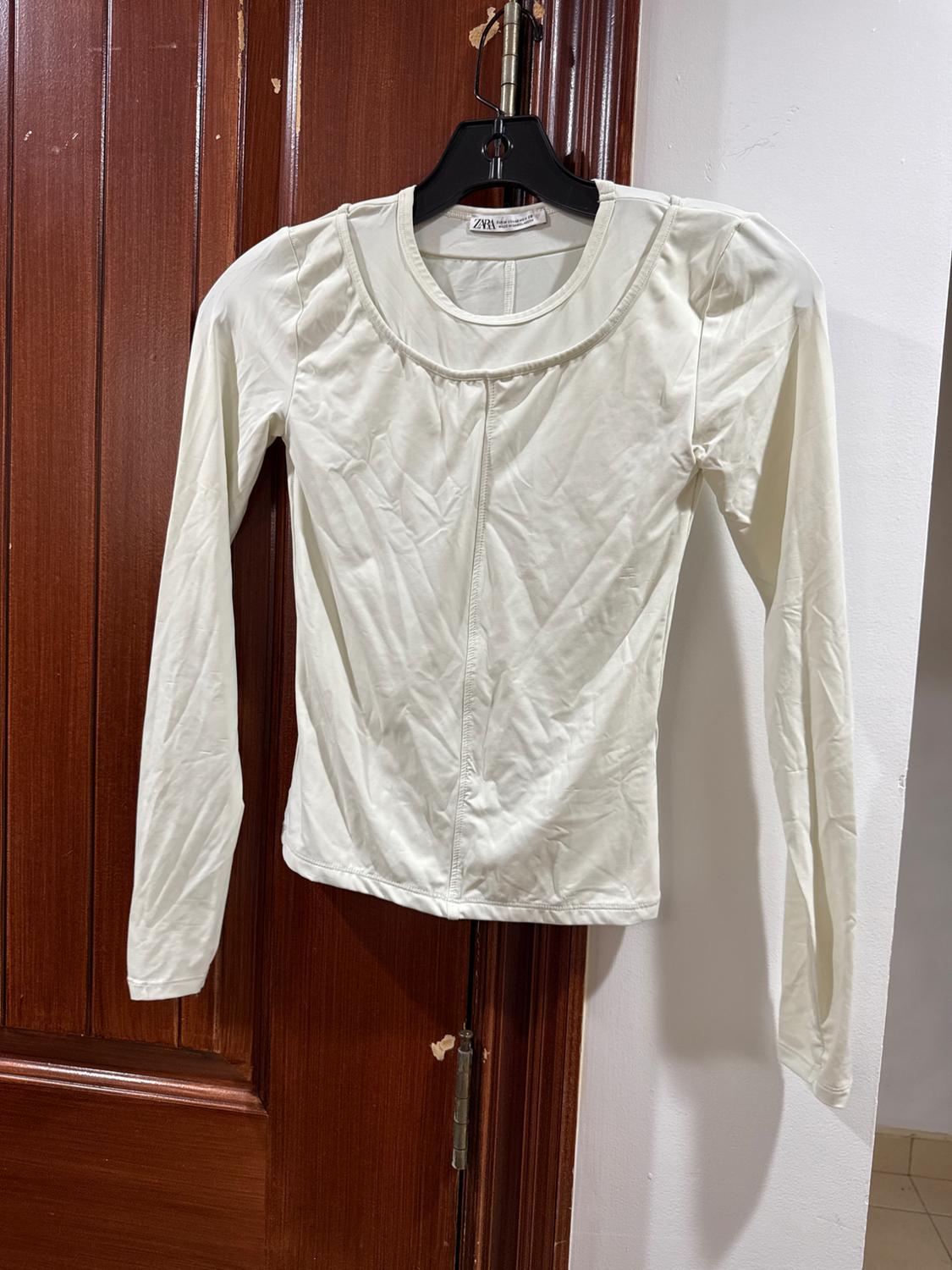 Long-sleeved white shirt hanging on a black hanger over a wooden door. Tag visible on the collar.