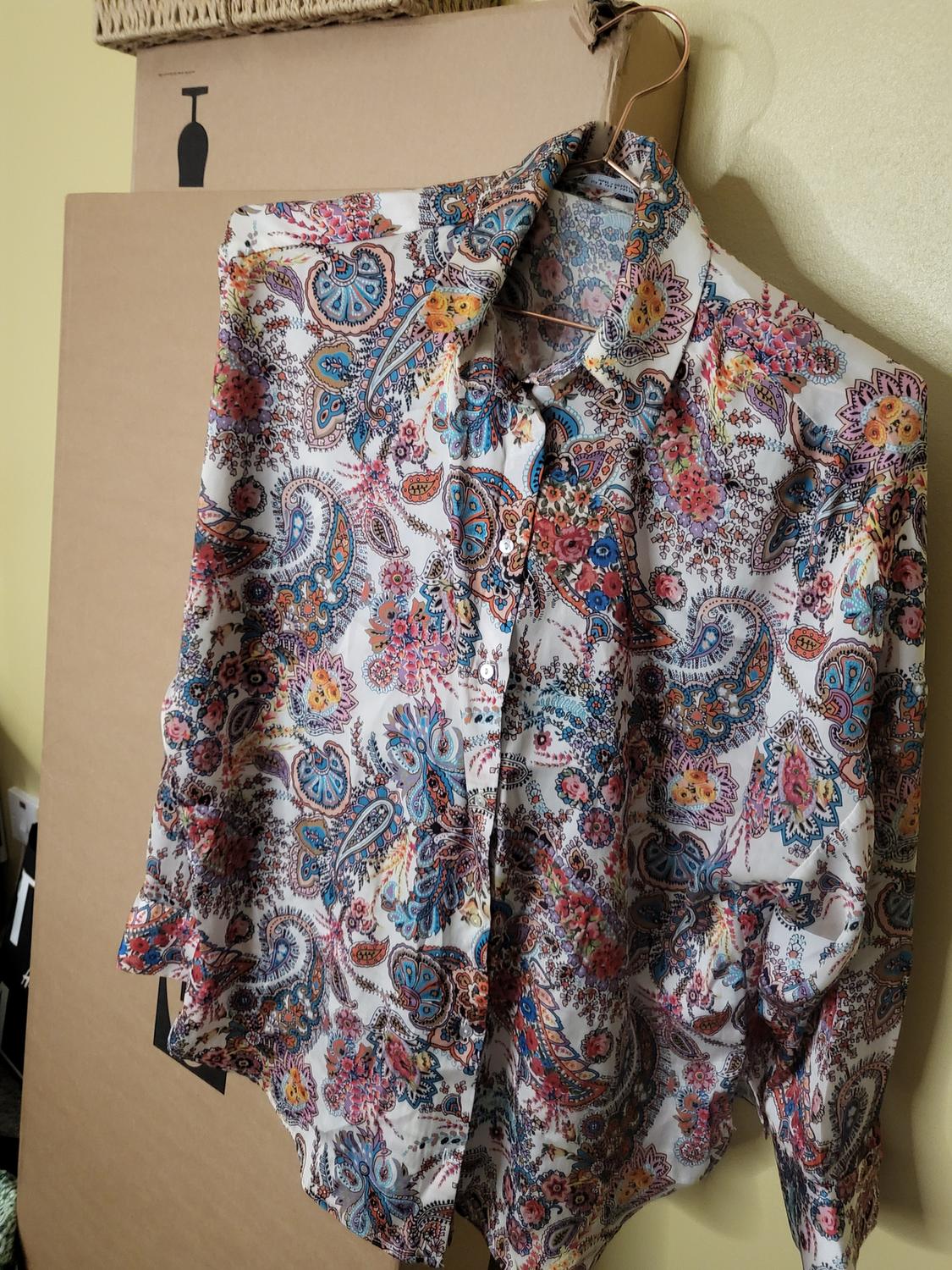 Multicoloured paisley print long-sleeved shirt hanging on a hanger, against a background of cardboard boxes.