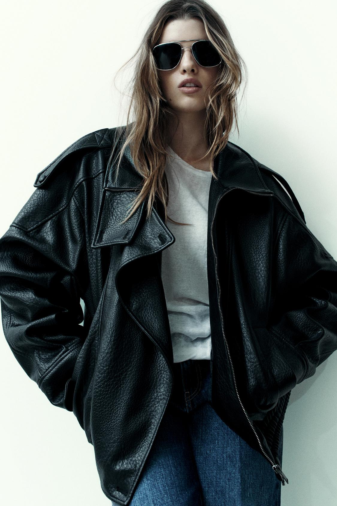 "Outfit consisting of a black jacket with a high neck, long sleeves and side pockets, over a white t-shirt and blue jeans."