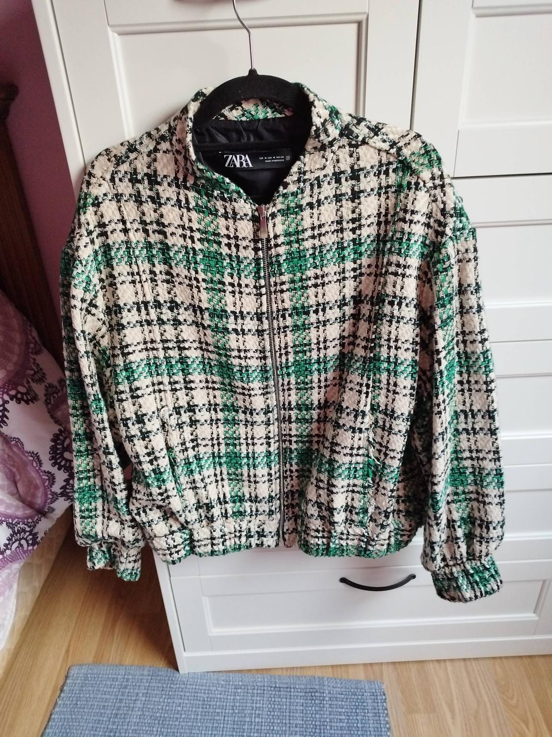 Green and black checked jacket hanging on a black hanger in front of a white wardrobe. Visible label: ZARA.