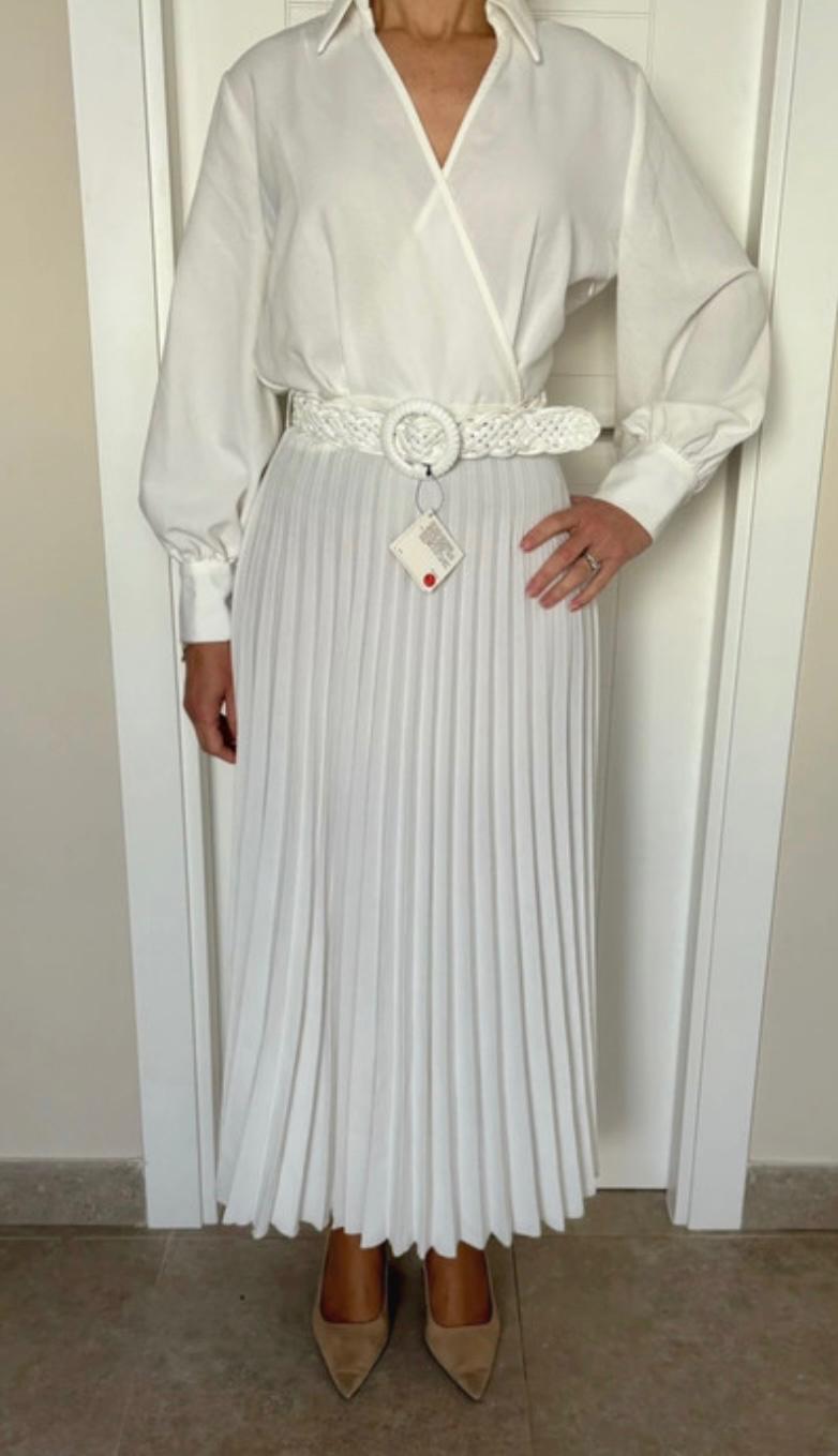 Woman in a white long-sleeved blouse, white pleated skirt, and braided belt. She is wearing beige high heels. Label visible on the belt.