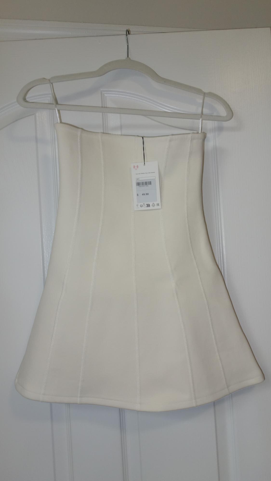 White flared skirt hanging on a white hanger over a door. Visible tag with price of $49.90.