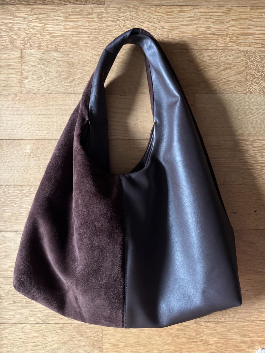 Dark brown shoulder bag with a design divided between suede texture and a smooth finish, resting on a wooden floor.