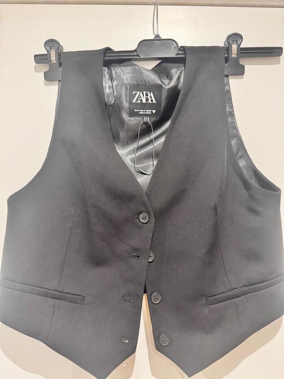 Black dress waistcoat hanging on a hanger, with a visible Zara label inside. Light background.