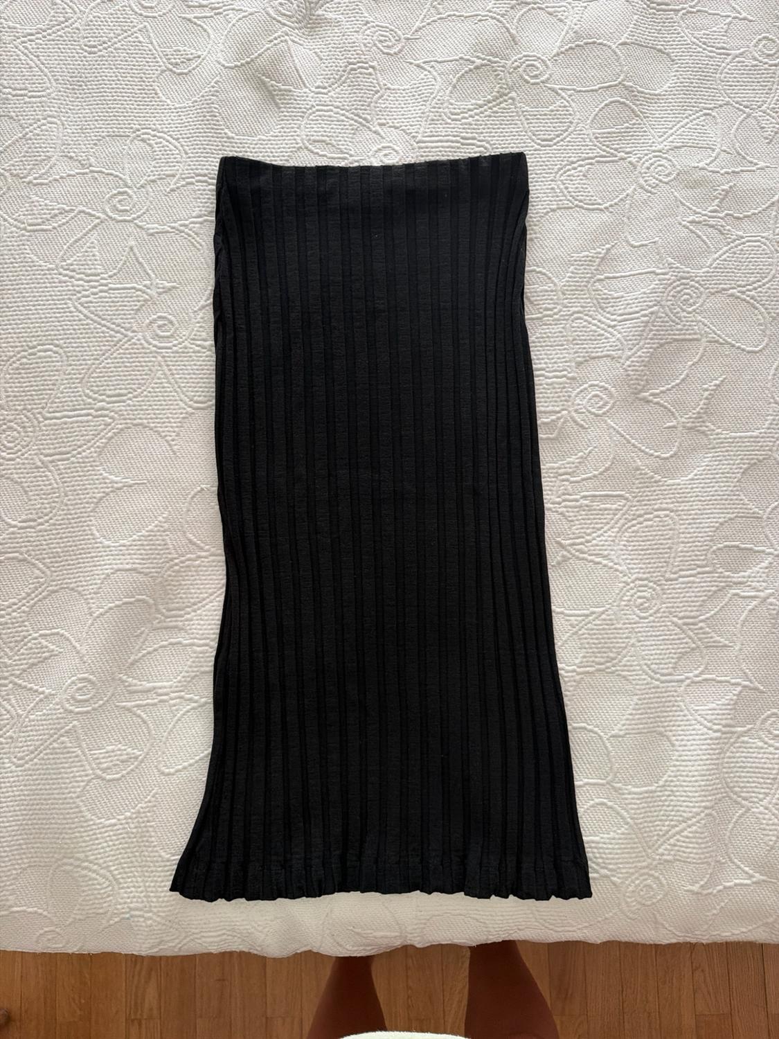 Black ribbed skirt on a white bedspread with a floral pattern. Seen from above, relaxed atmosphere, feet visible on a wooden floor.