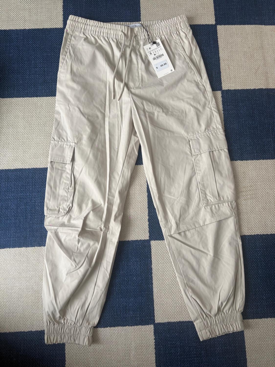 Beige cargo pants with an elastic waist and side pockets, on a blue and white checkered rug. Price tag visible.