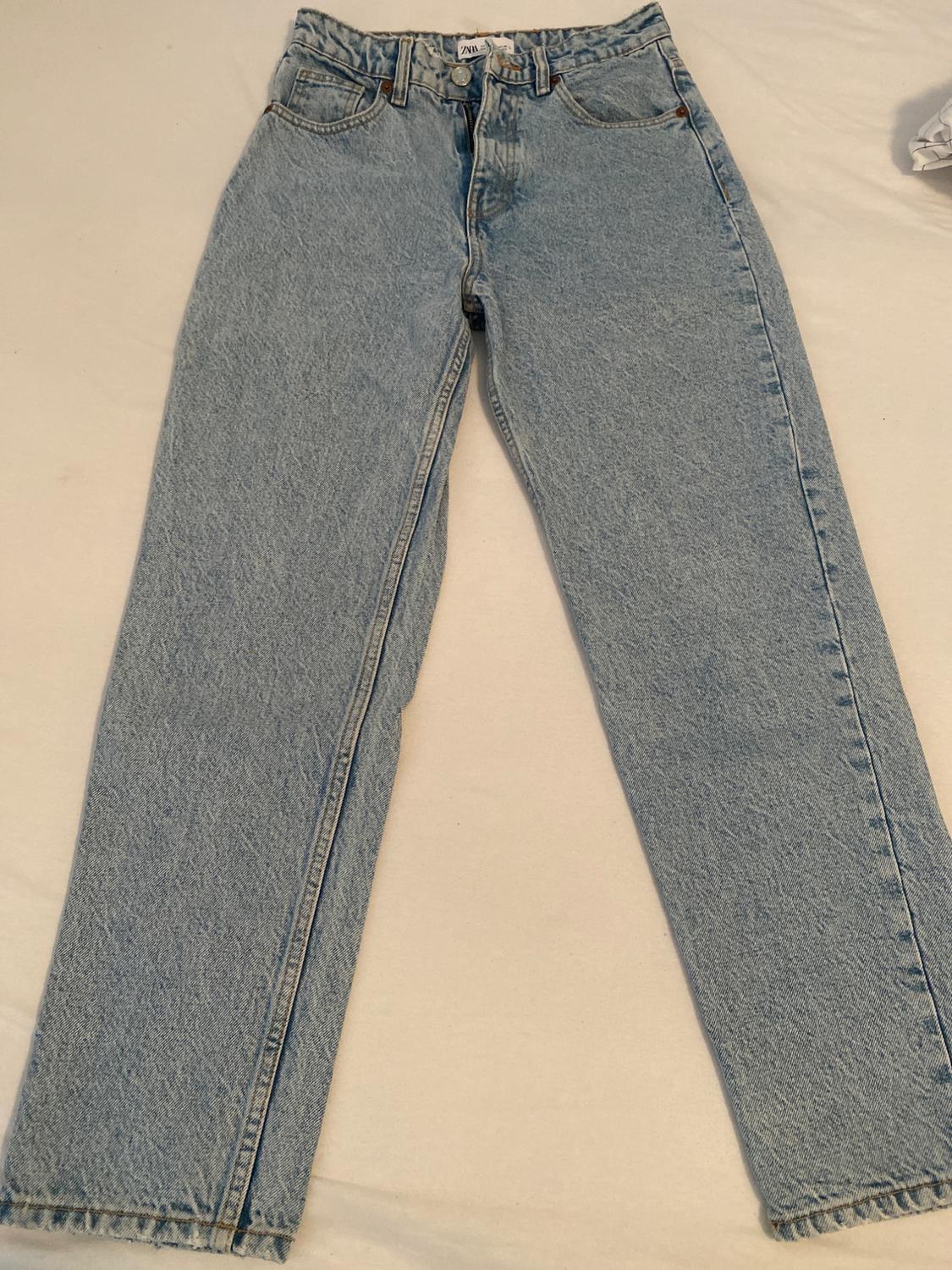 Light blue, high-waisted denim jeans laid out on a white sheet. Casual style with five pockets and a visible ZARA label.