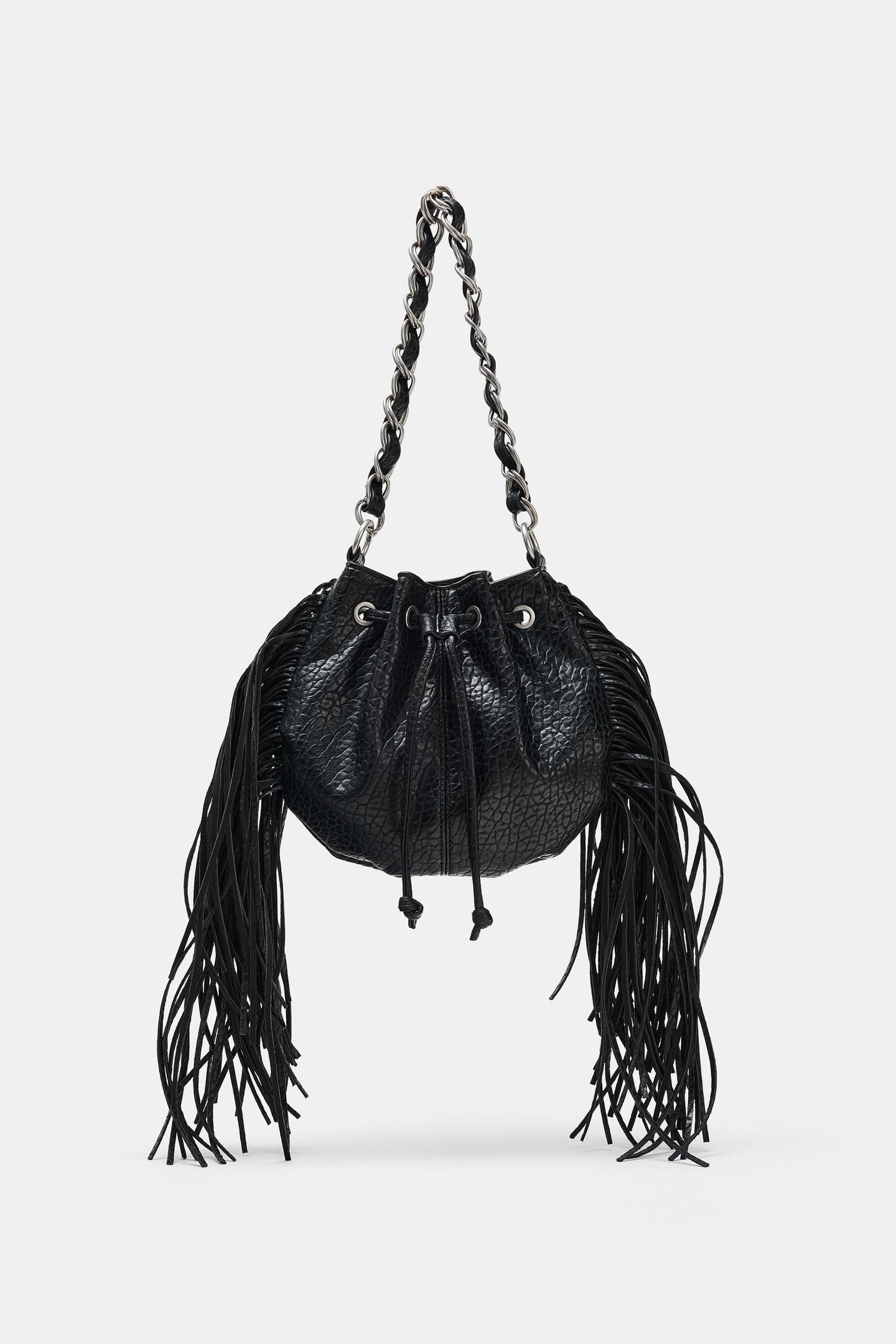 Front view of a black bag with a drawstring closure, long fringe on the sides, and an interwoven chain top handle.