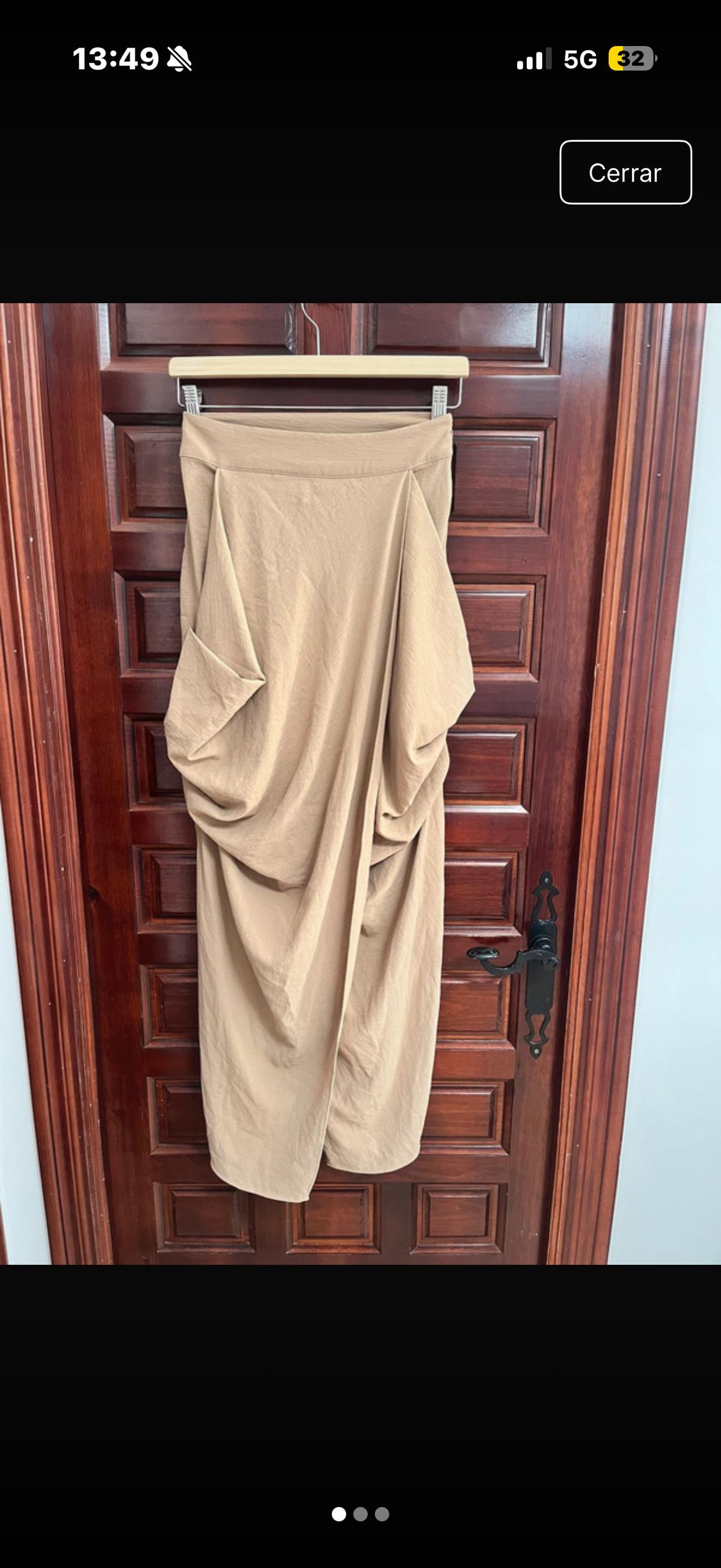 Beige draped skirt hanging on a dark wooden door. Phone screen displaying time 13:49 and 5G signal.
