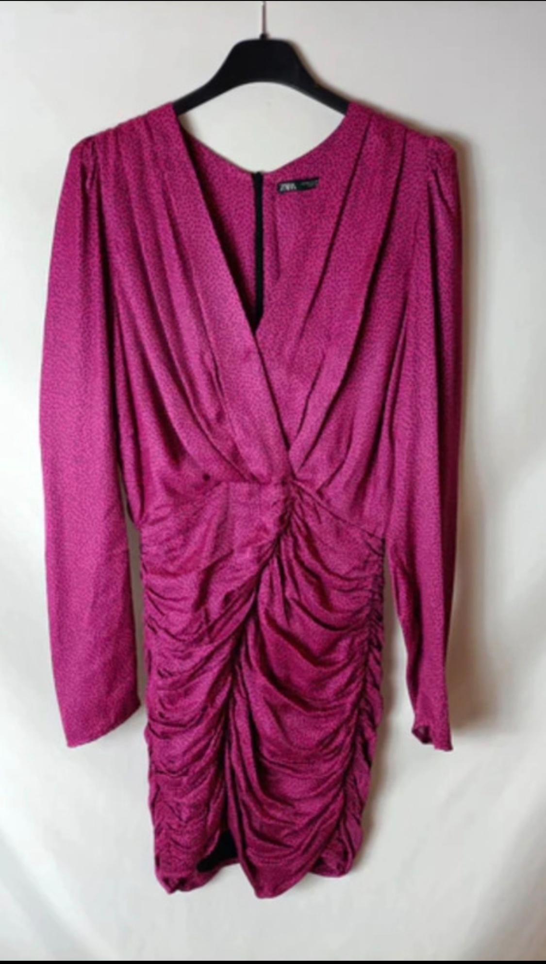 Fuchsia dress with front draping and long sleeves, hanging on a black hanger against a white background.