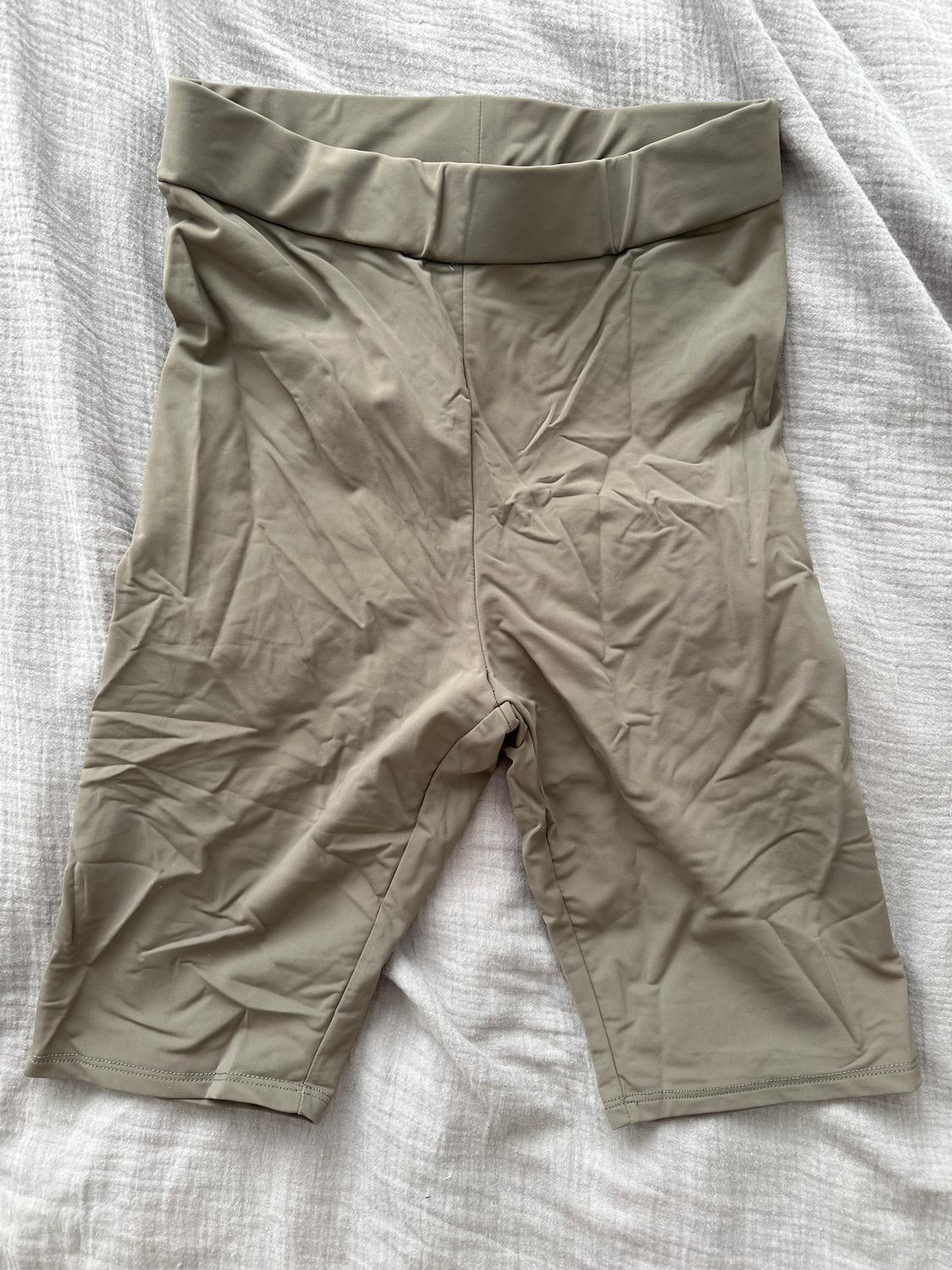 Light beige shorts with a wide waistband, placed on a textured white fabric.