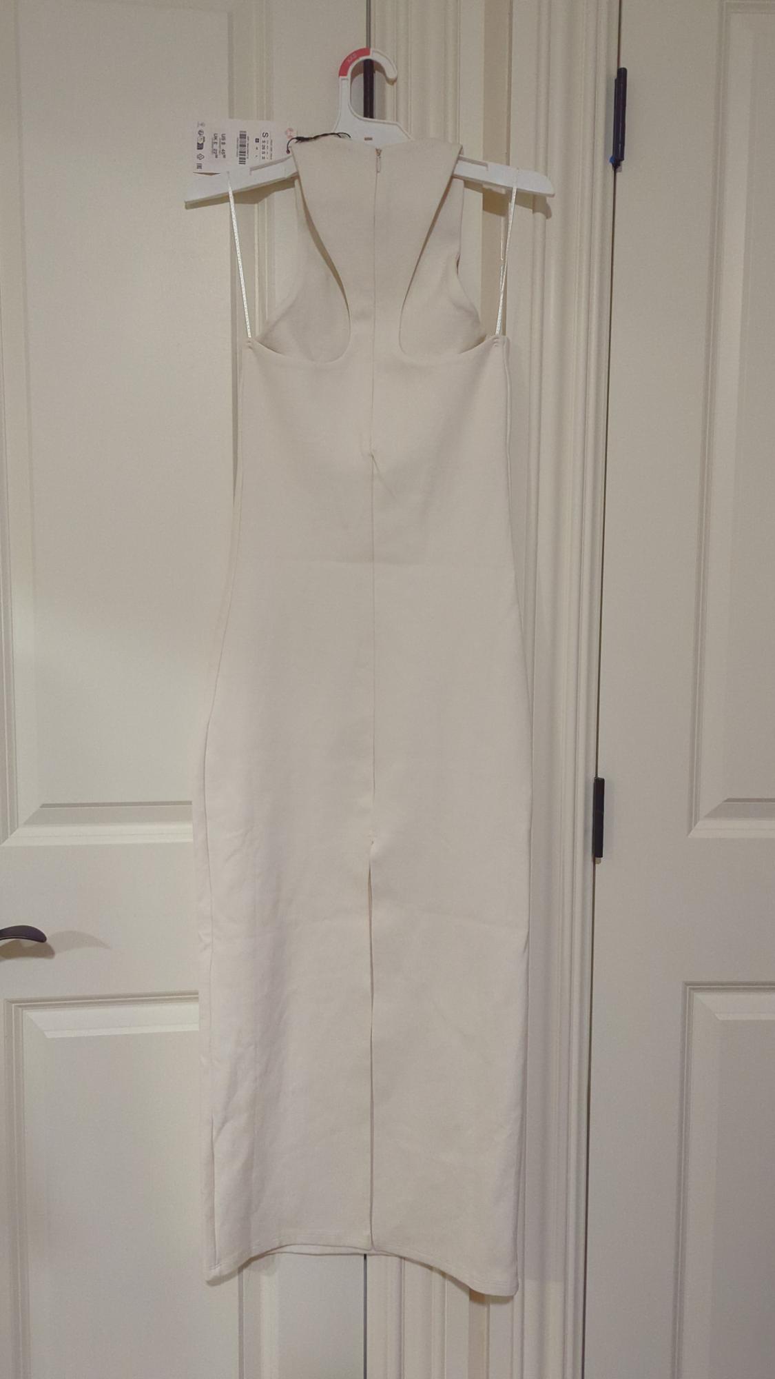 Sleeveless white dress hanging on a hanger in front of a white door. Label visible in the top left.