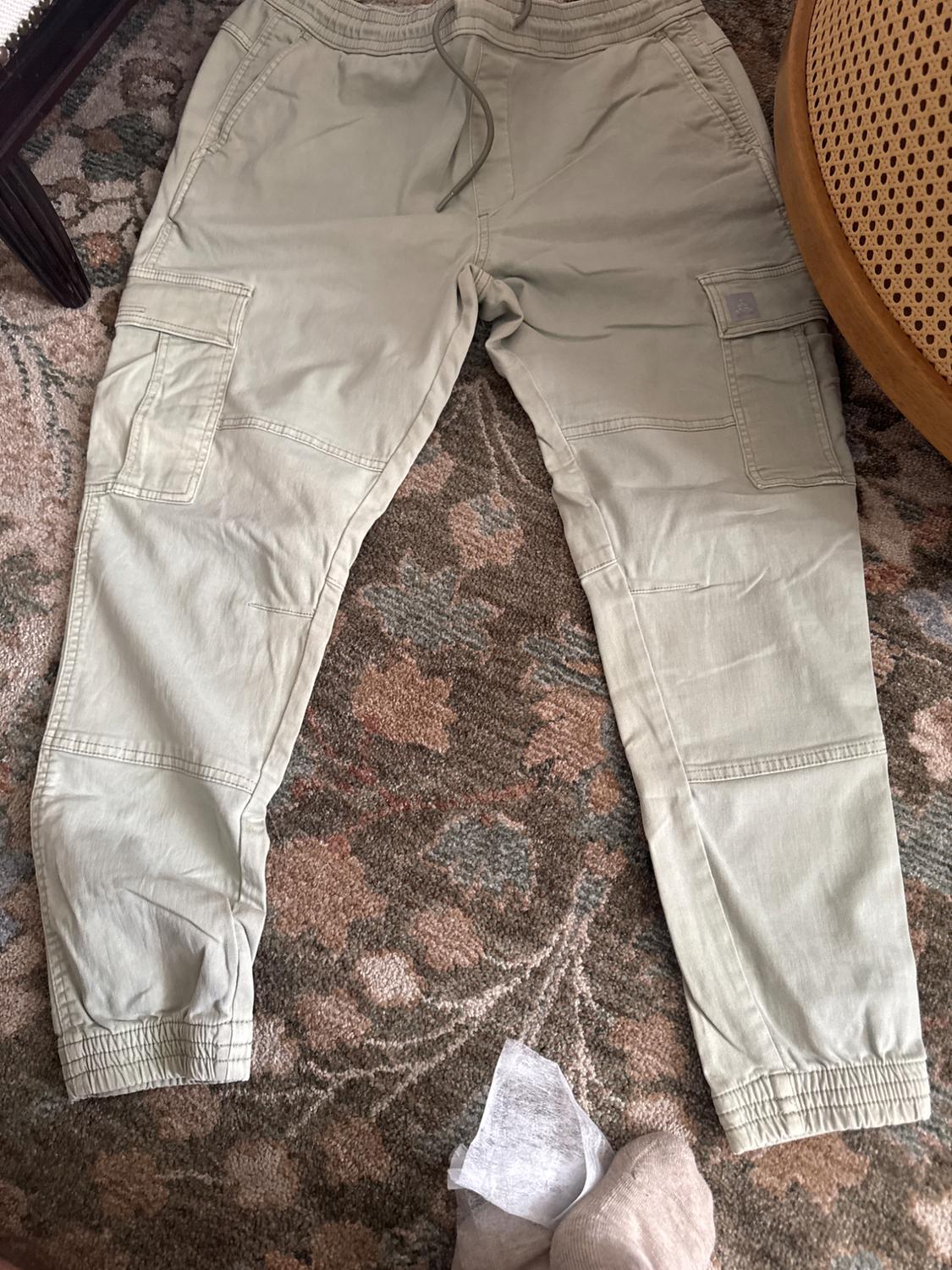 Beige cargo trousers with side pockets and an elasticated waist, placed on a floral-patterned rug.