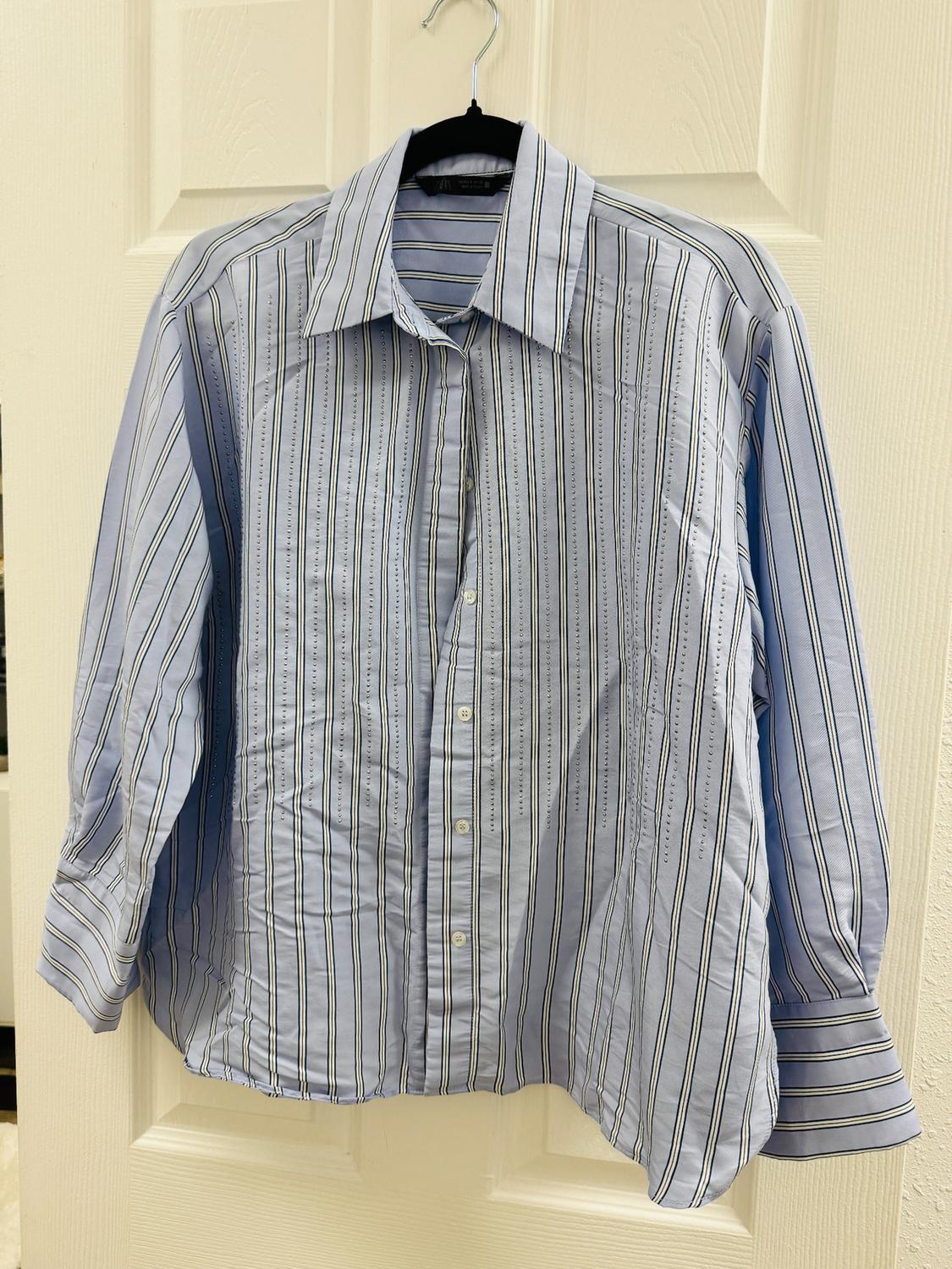Blue and white striped shirt hanging on a black hanger over a white door. Long sleeves and buttons down the front.