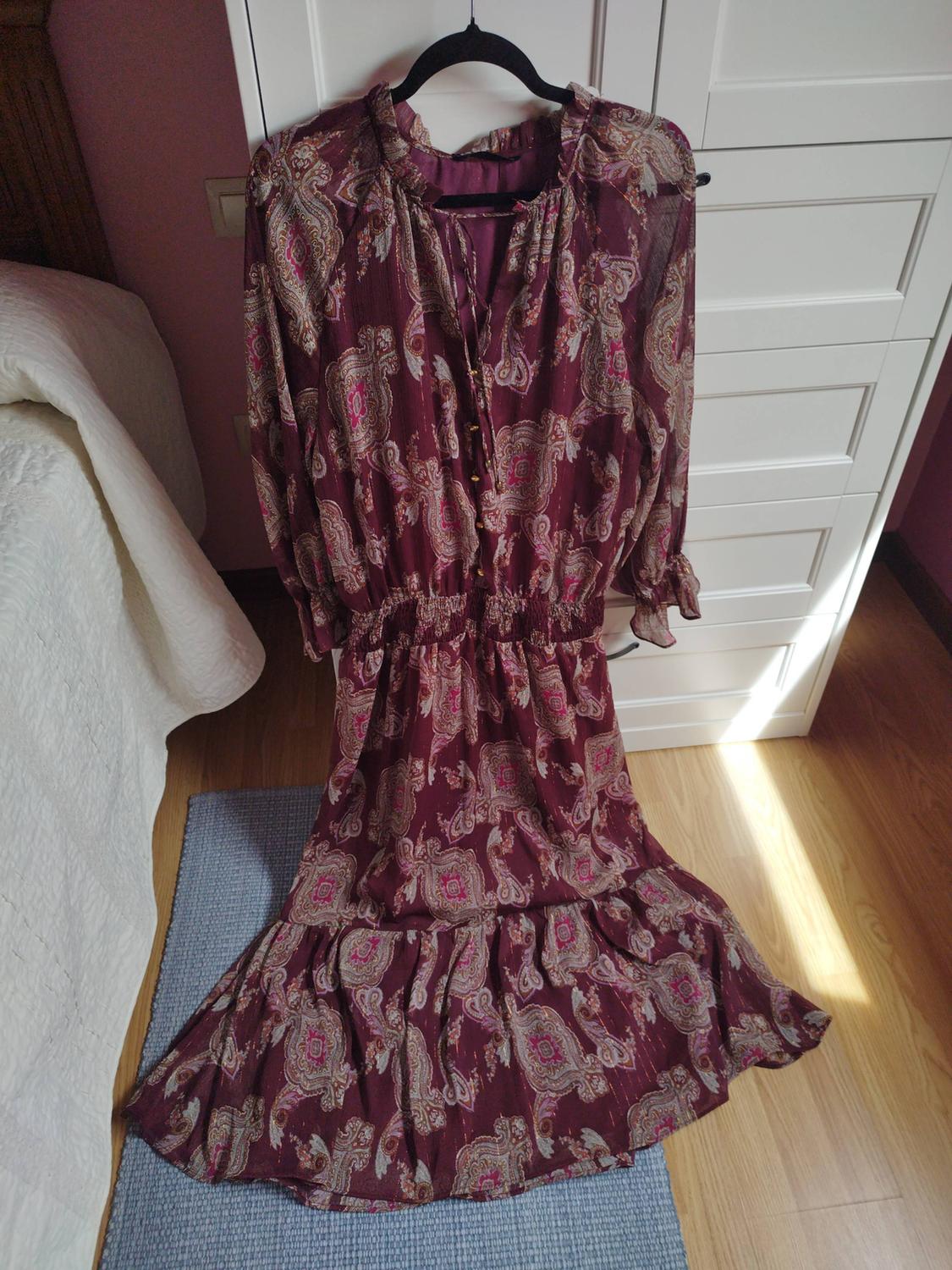 Burgundy paisley print maxi dress with an elasticated waist, hanging in a white wardrobe inside a sunny bedroom.
