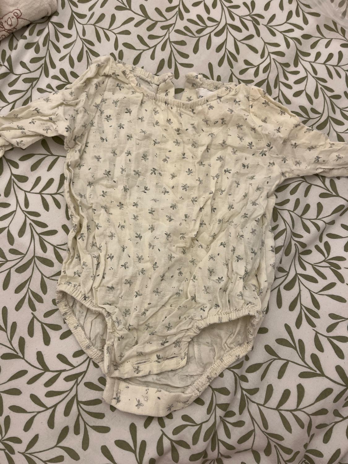 White, long-sleeved babygrow with a pattern of small grey flowers, on a white quilt with a green leaf design.