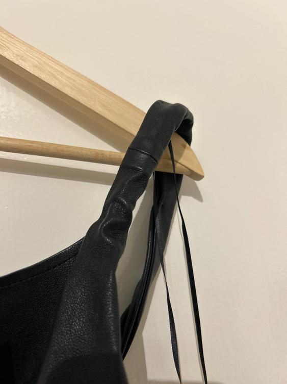 Black dress strap hanging on a wooden hanger against a white background. Detail of dress texture and ribbons.