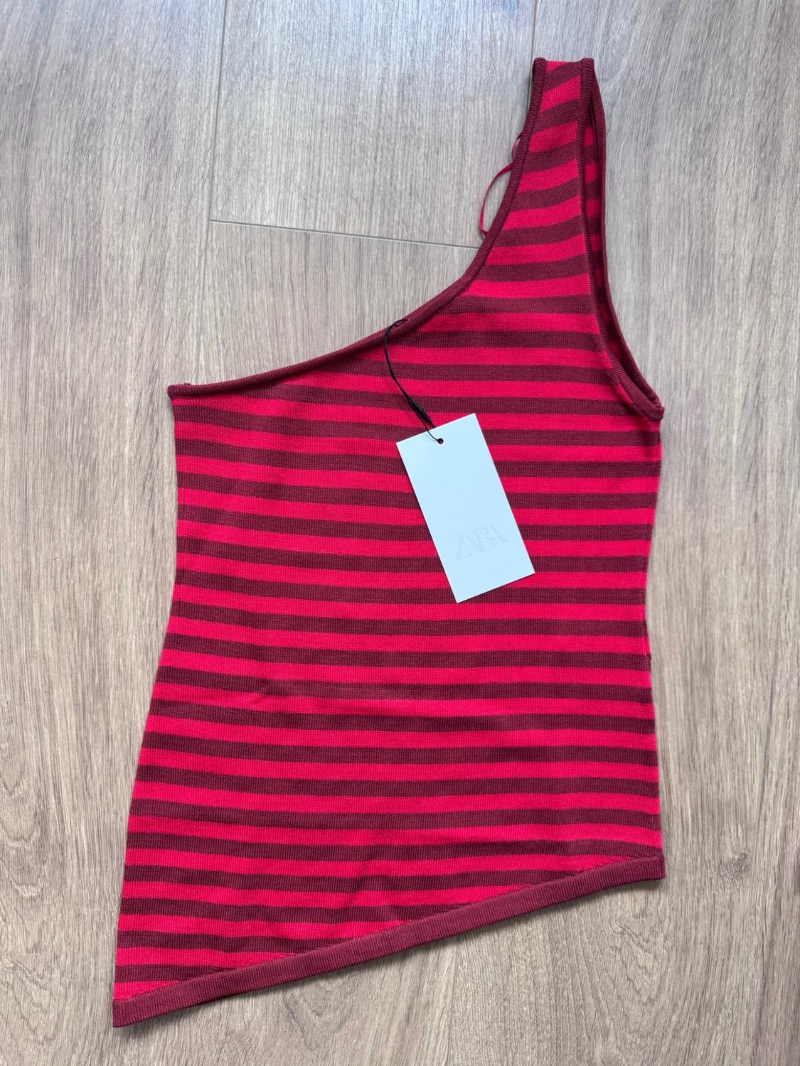 Asymmetric one-shoulder top with red and burgundy horizontal stripes on a wooden floor. Label with ZARA text.