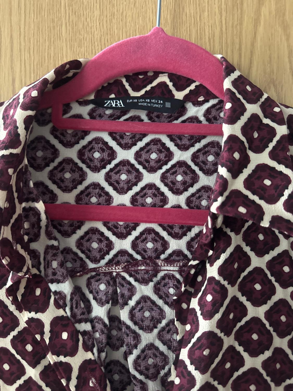 Burgundy and cream geometric print shirt on a pink hanger. Text: ZARA EUR XS USA XS MEX 24 MADE IN TURKEY.