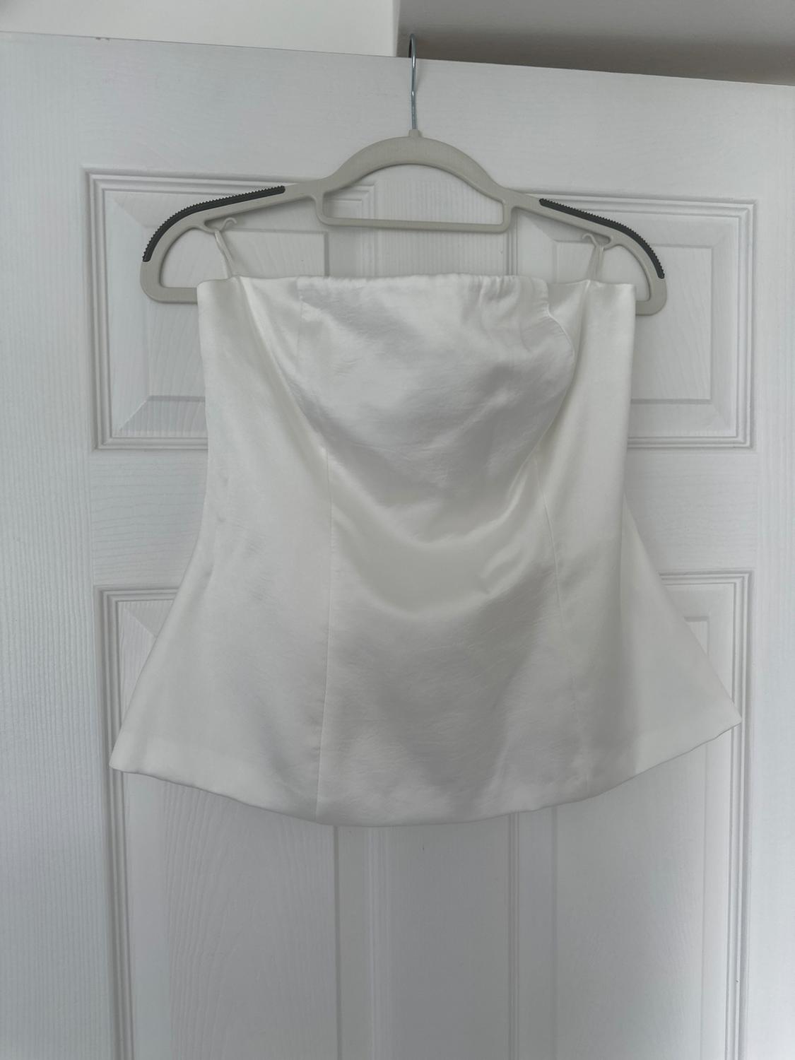 Strapless white satin top hanging on a grey hanger over a white panelled door.
