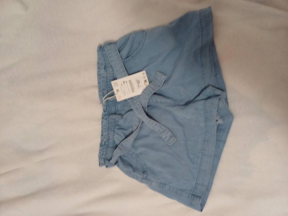 Light blue fabric shorts with matching belt, visible hang tag, on a white background.