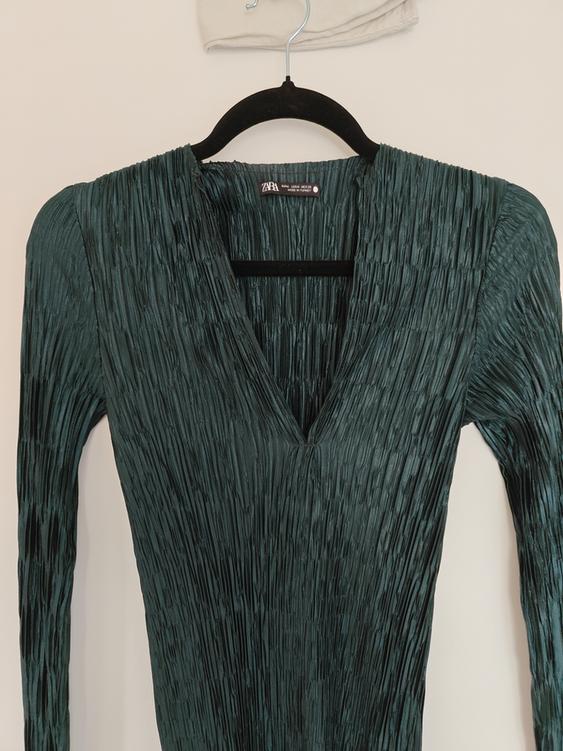 Pleated green dress with V-neck, hanging on a black hanger. Visible label with text: "ZARA". White background.