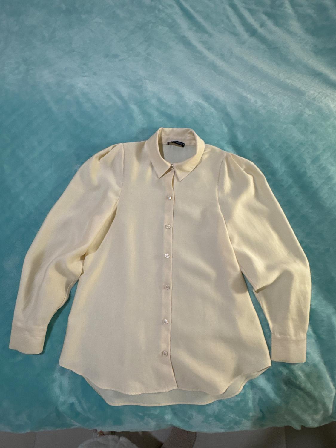 Cream long-sleeved shirt with buttons, placed on a light blue quilt.
