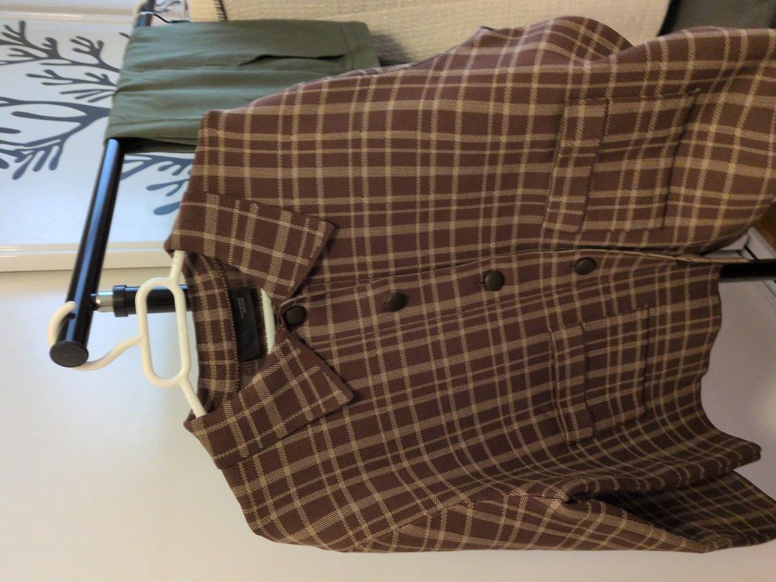 Brown checked jacket hanging on a clothes rack next to green trousers. Background with black branch design.
