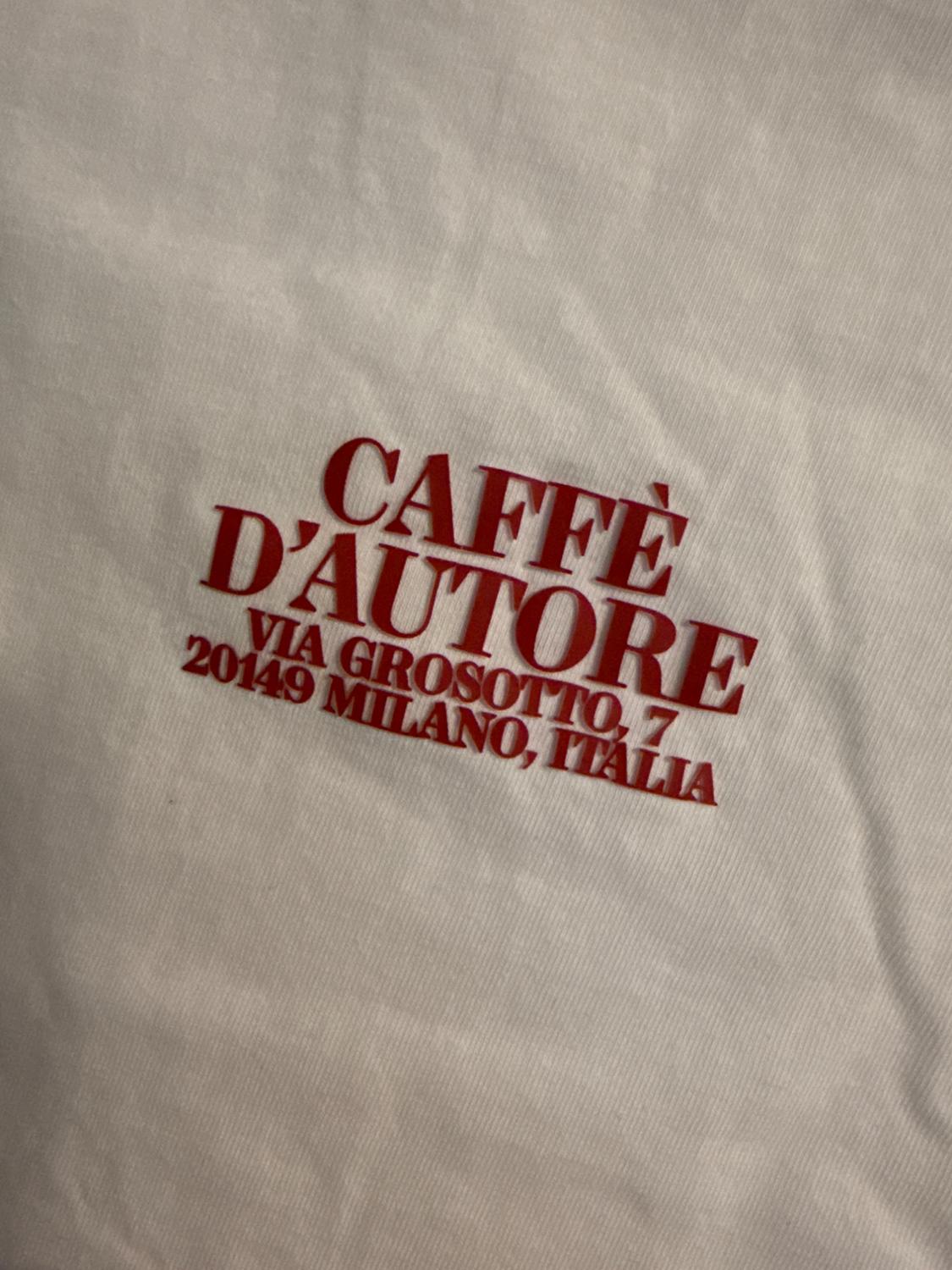 Red text on a white T-shirt that reads: "CAFFÈ D'AUTORE VIA GROSOTTO, 7 20149 MILAN, ITALY".