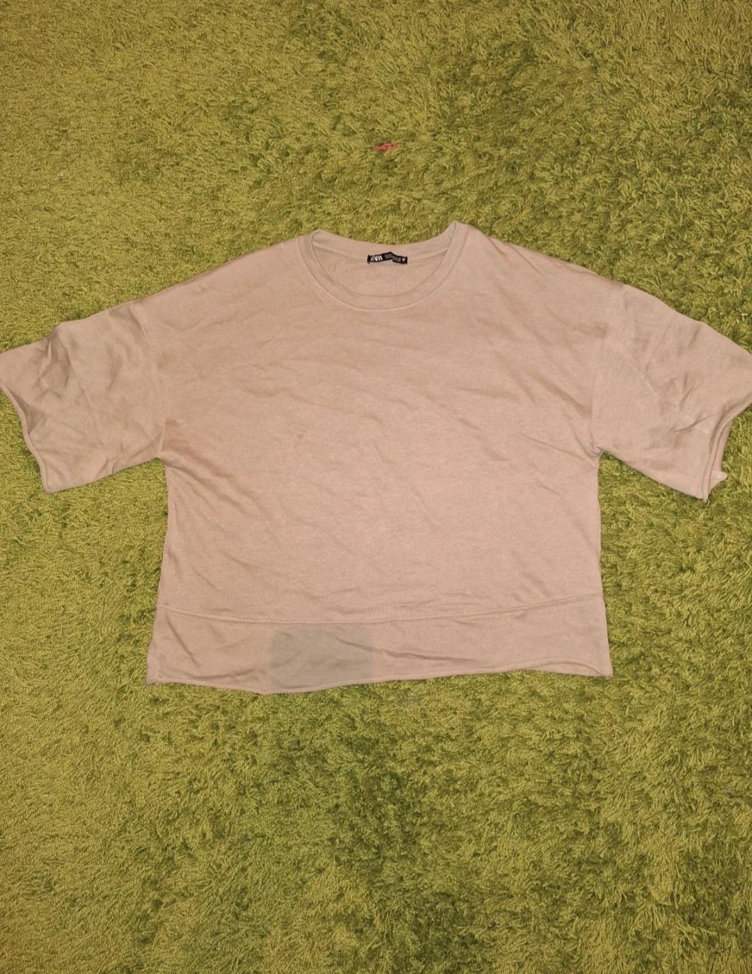 Beige short-sleeved T-shirt on a green rug. Visible label on the collar.